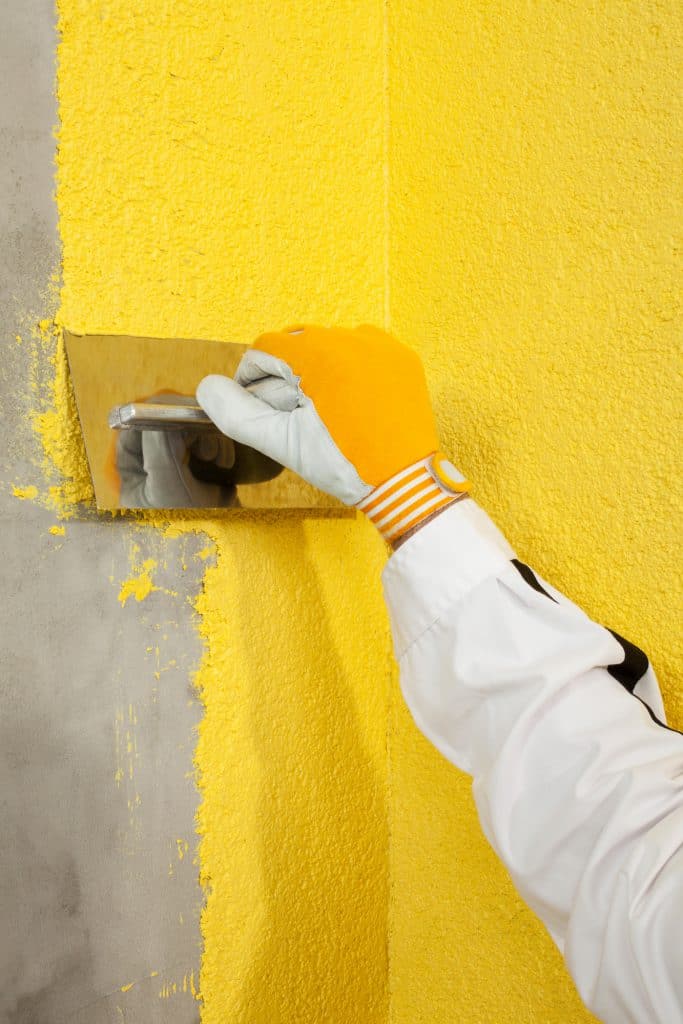 Using a trowel to spread color plaster onto the corner of a wall