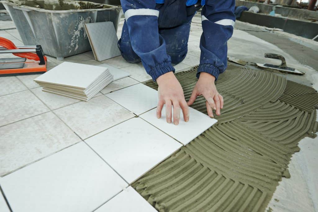 A contractor laying tile and adhesive directly onto a concrete subfloor