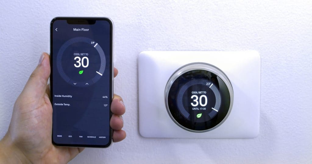 A person with a iPhone 11 Pro Max using the Nest App near a wireless Nest Learning Thermostat