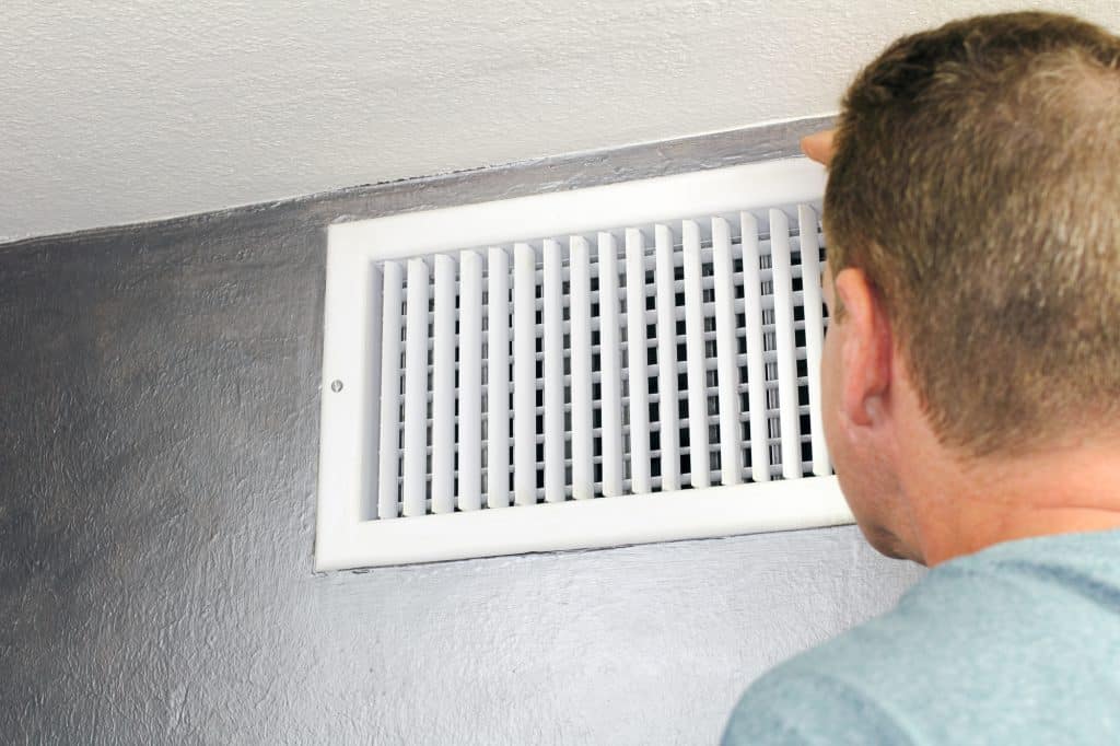 Someone looking at an air vent in a room
