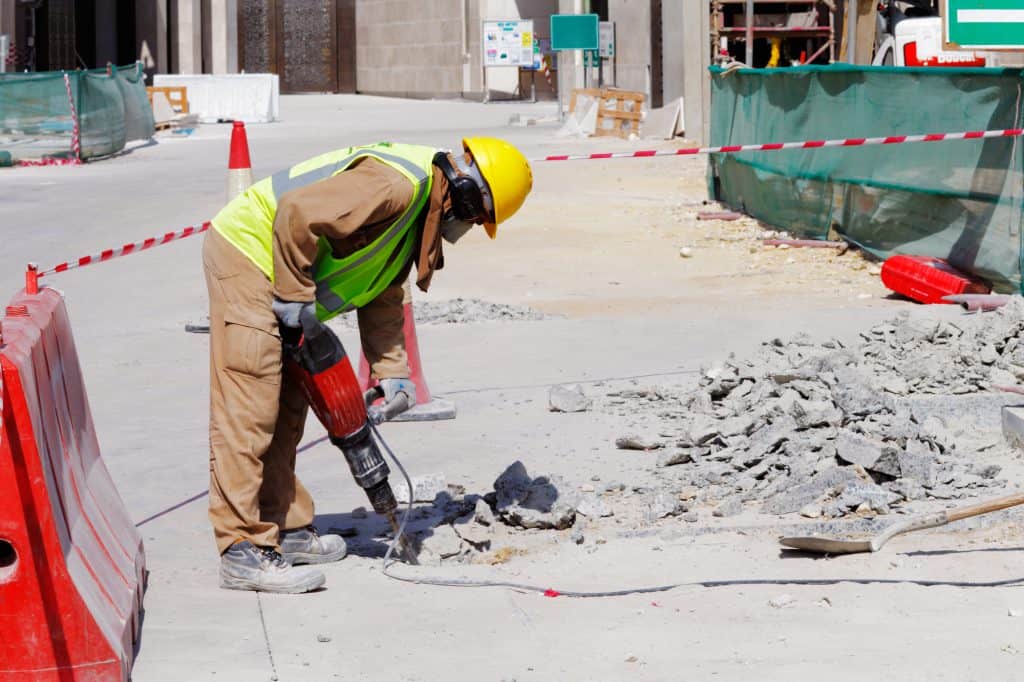 A laborer uses a jackhammer to break up a concrete area