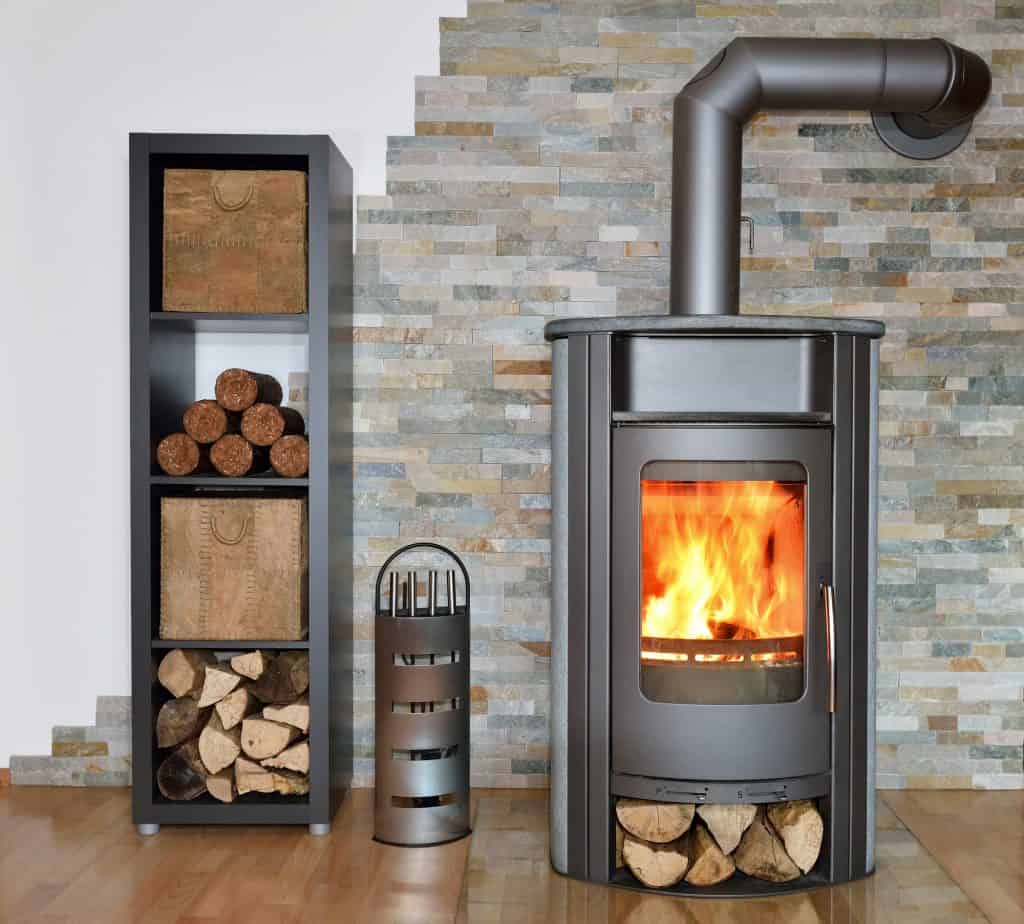 A wood fired stove with stacked wood beside it